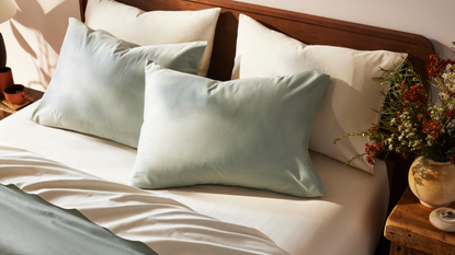 a bed with white and sage sheets next to a wooden nightstand with flowers